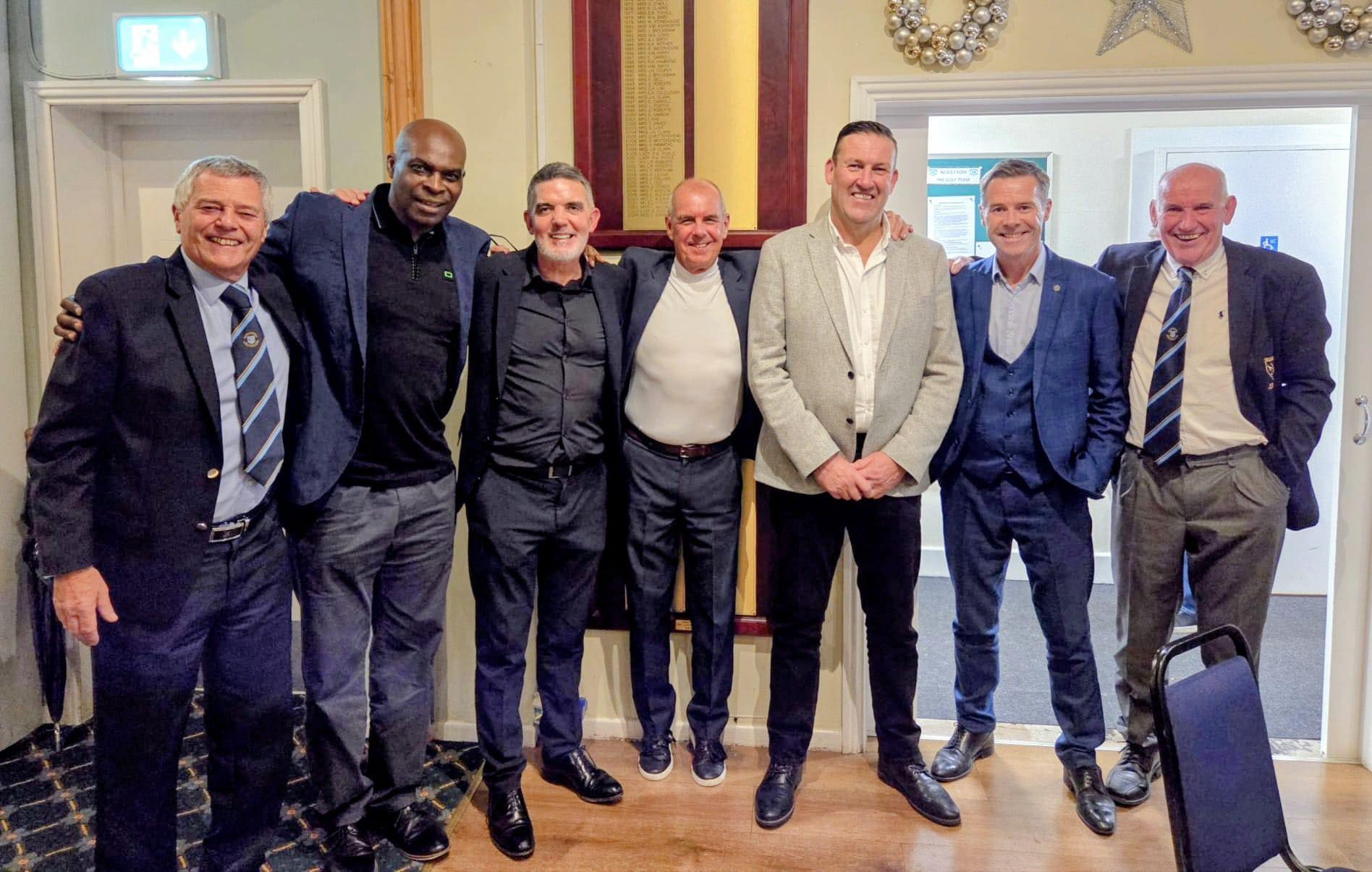Golf course putting green with sand bunker and trees under clear blue sky.