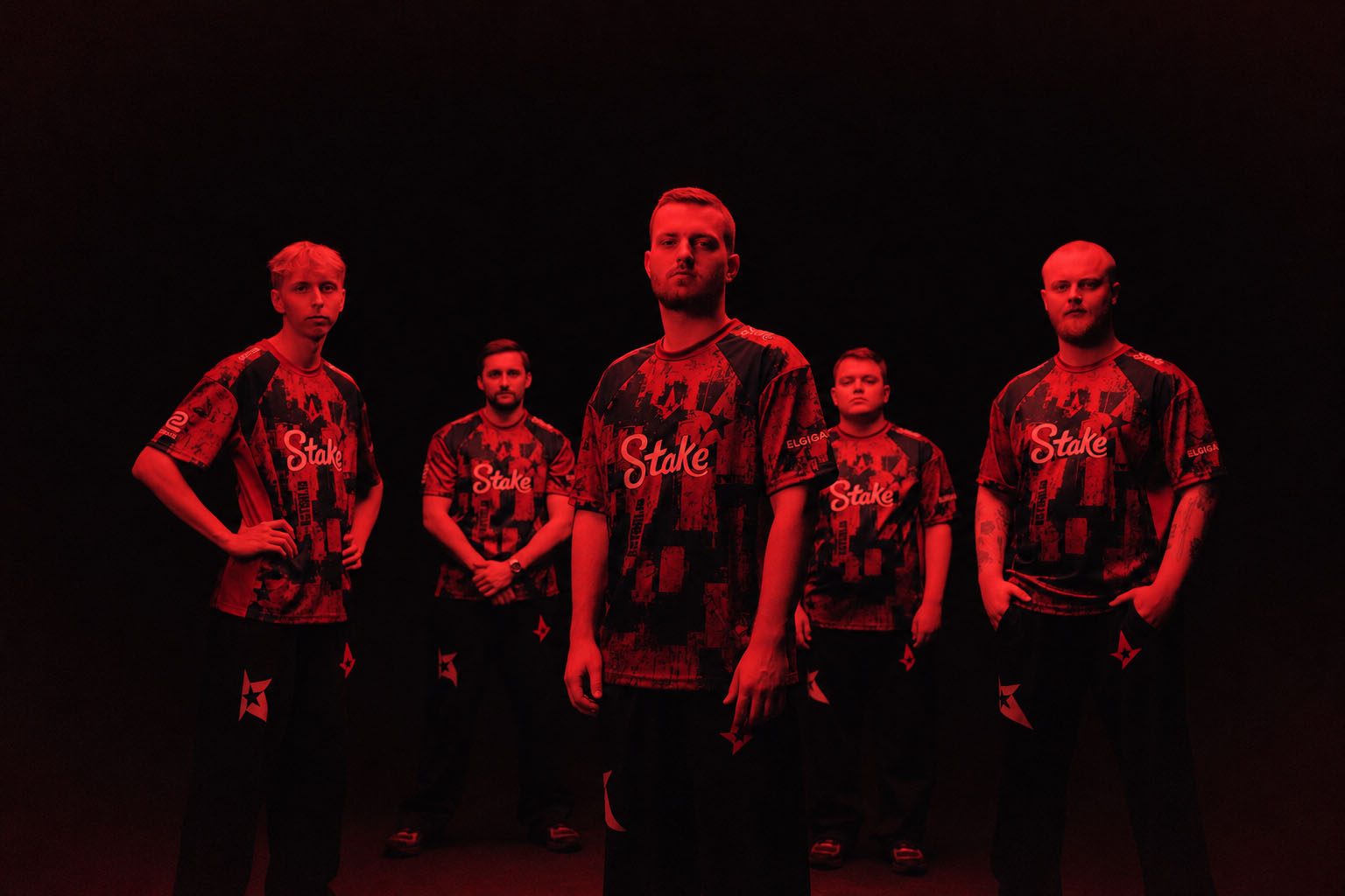 Five Astralis team members in team jerseys against a dark background with a red overlay.