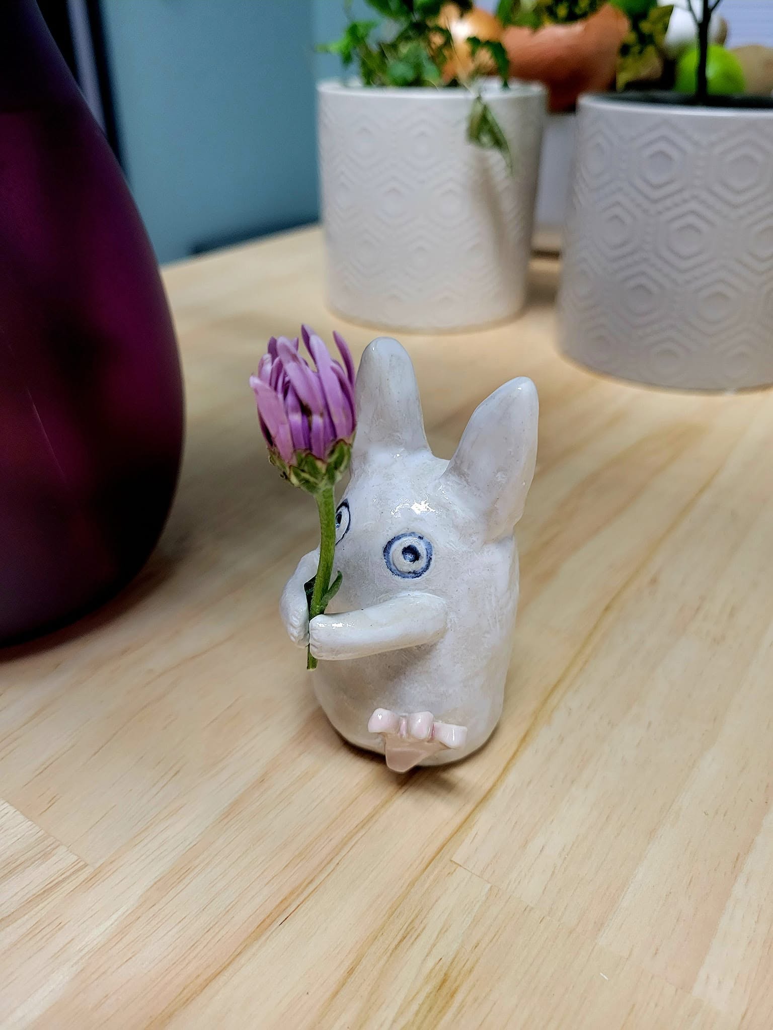 A hand-sculpted mini-Totoro holds a flower bud as if they are marching across a butcher block counter.