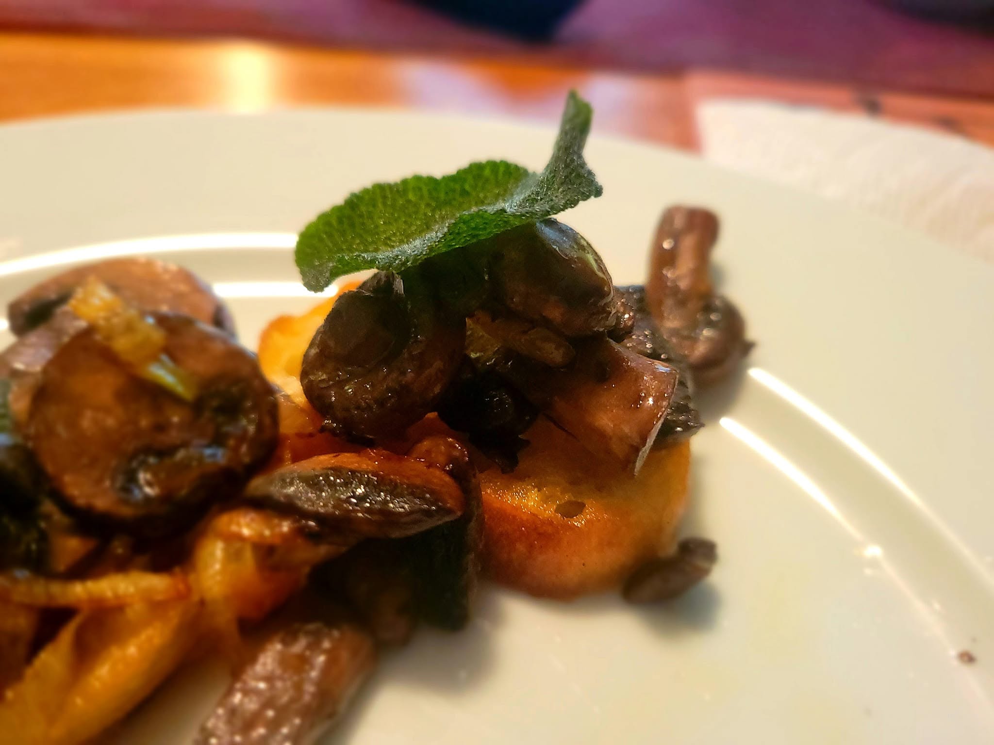A fried sage leaf sits atop a sauteed mushroom on crisp toast.