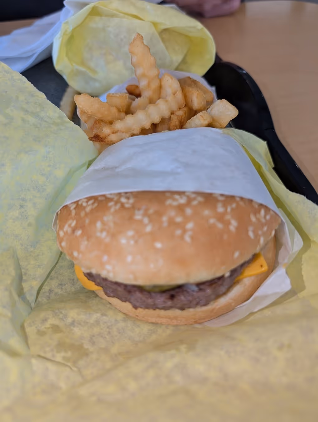 A cheeseburger with fries on a paper wrapper.