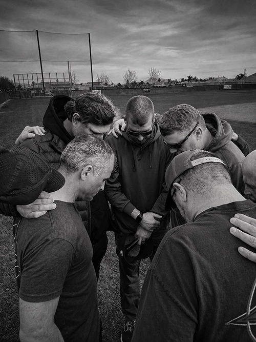 Black Gold Baseball coaches gathered together in prayer on the field