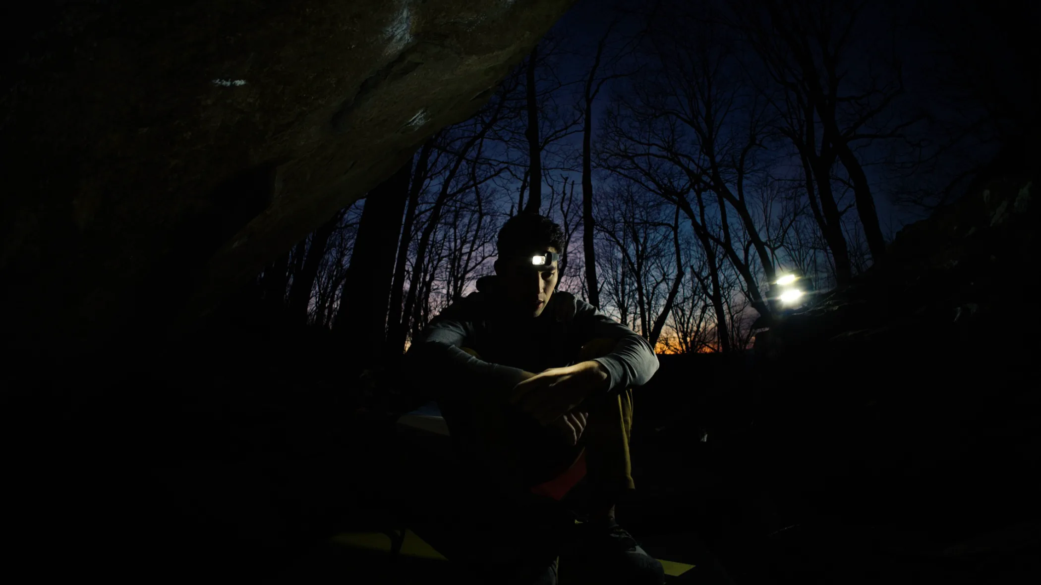 Climber resting under a boulder at dusk, headlamp on