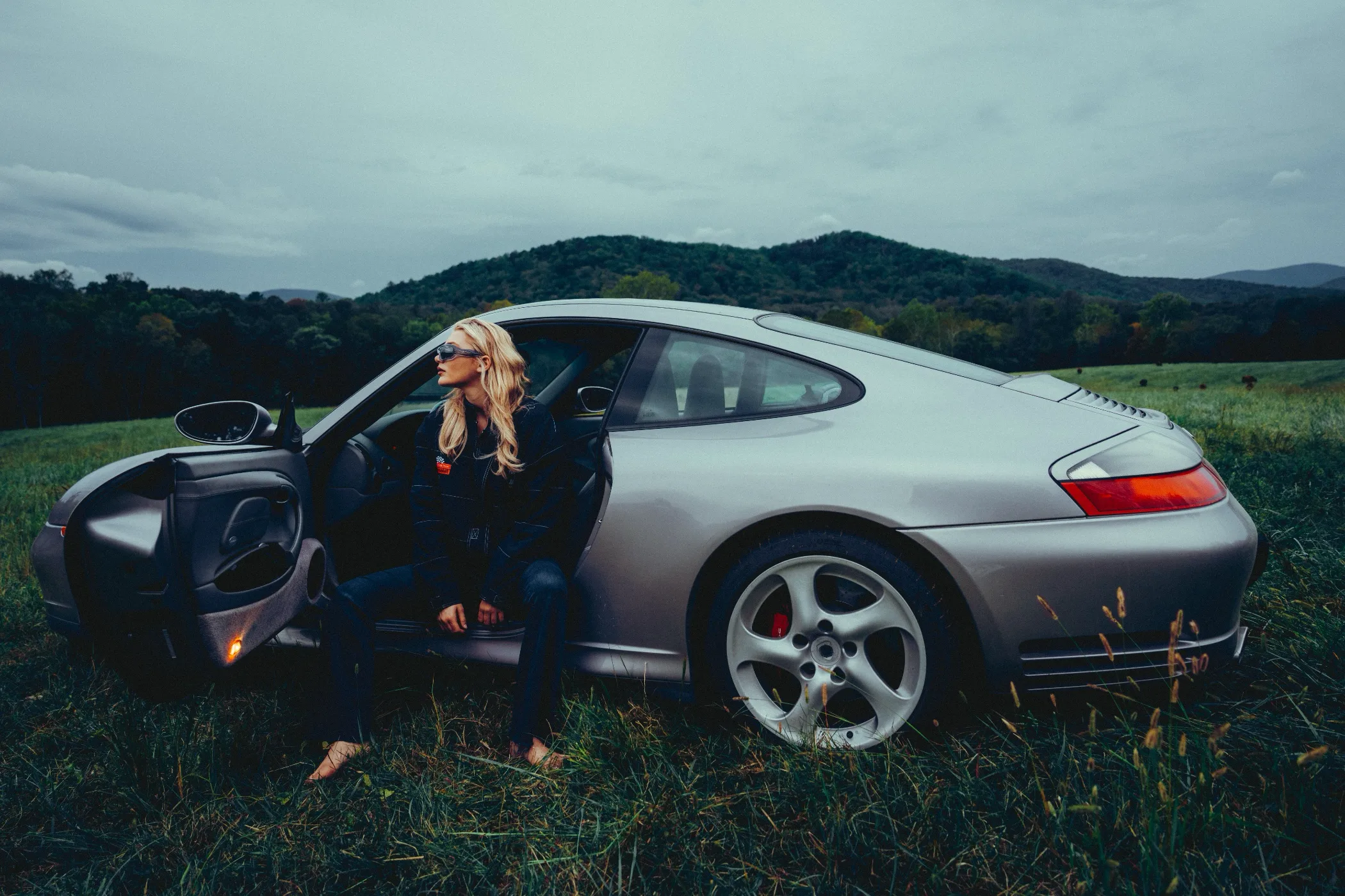 Model Bebe Soloviev beside a silver Porsche 911 in a mountain field