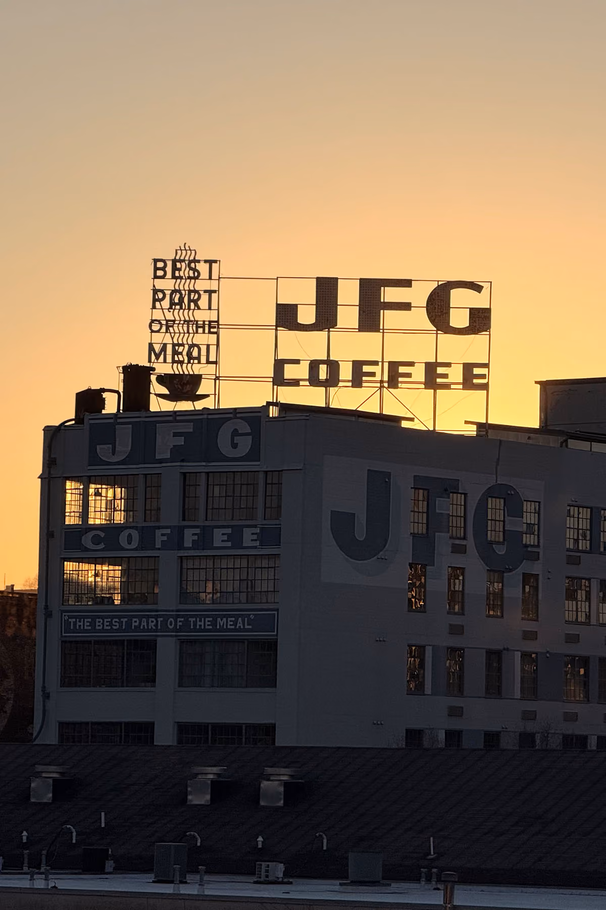 A metal sign on a building that reads JFG coffee with a sunset in the background