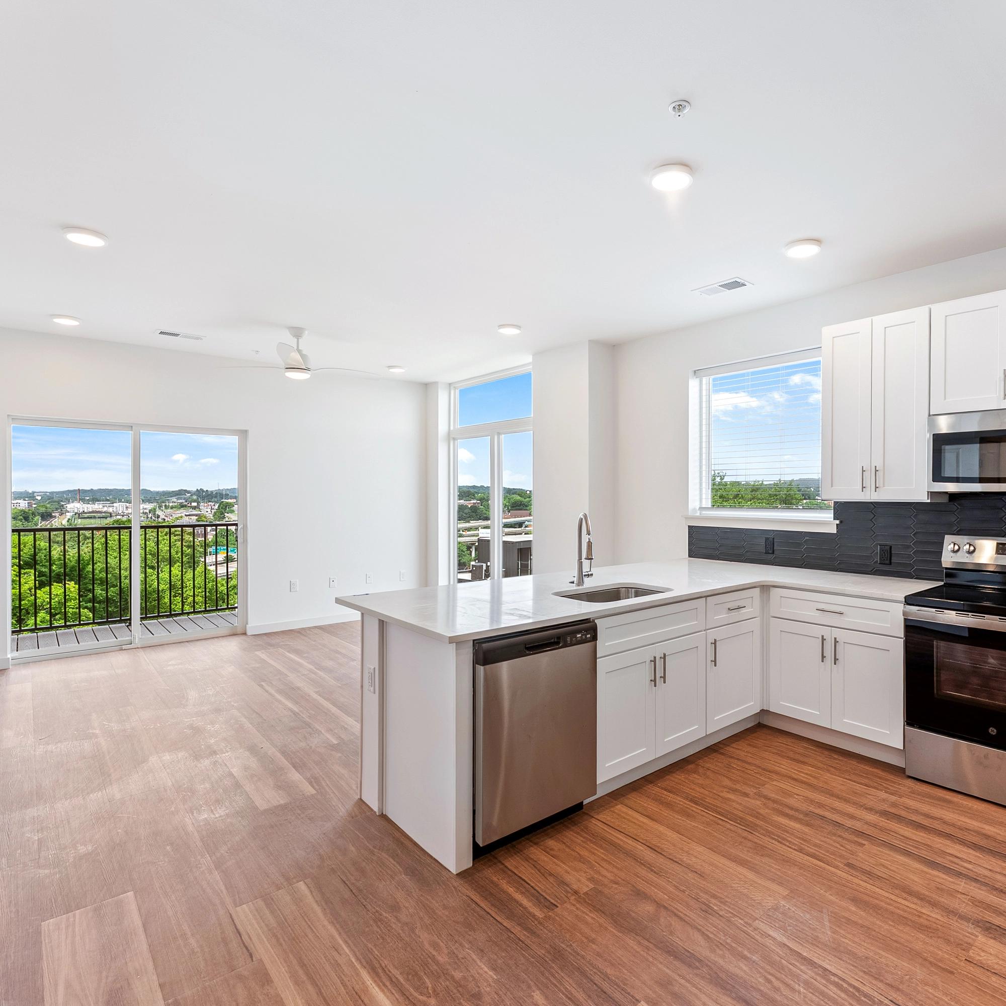 Modern kitchen with white cabinets, stainless steel appliances, island, wood floor, and balcony view.