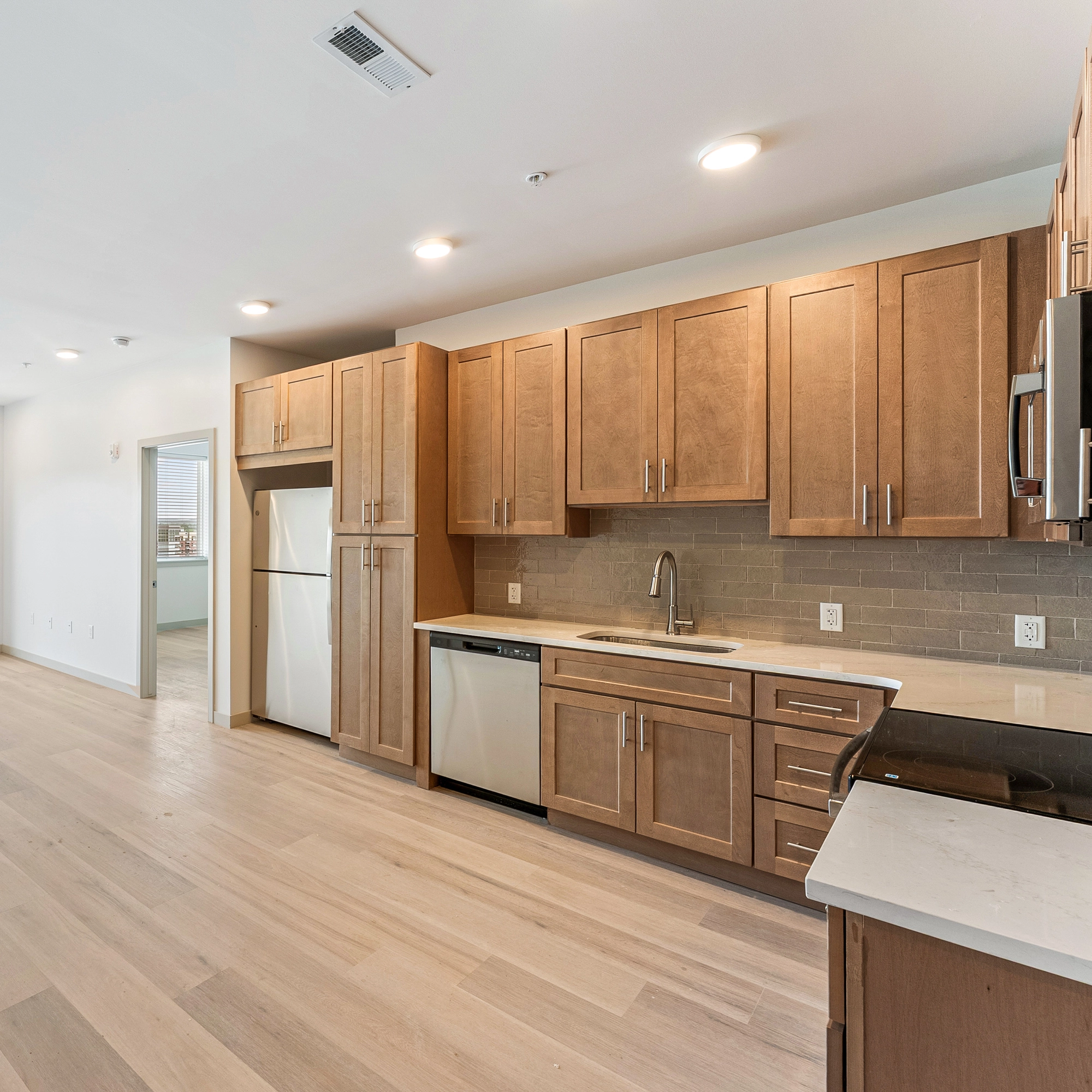 Modern kitchen with light wooden cabinets, stainless steel appliances, and light wood flooring.