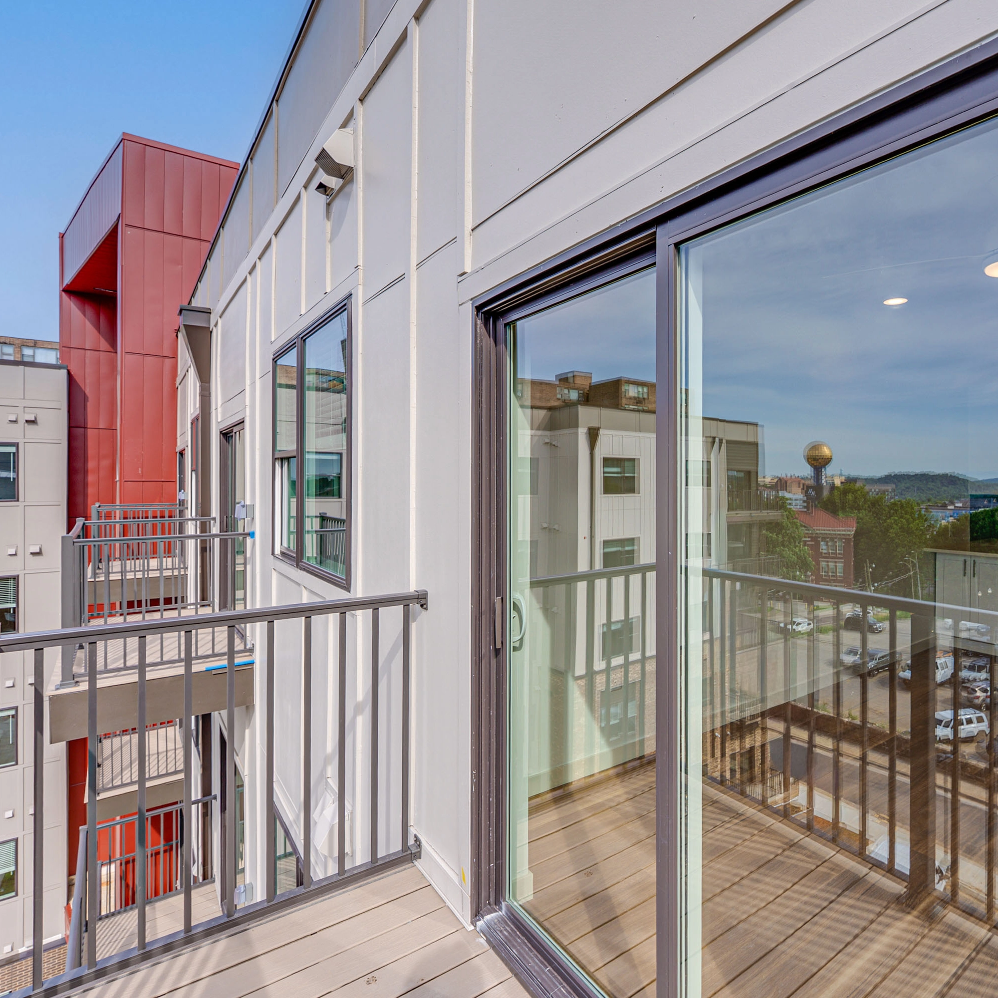 Apartment balcony with metal railings and sliding glass door, cityscape reflected in glass.
