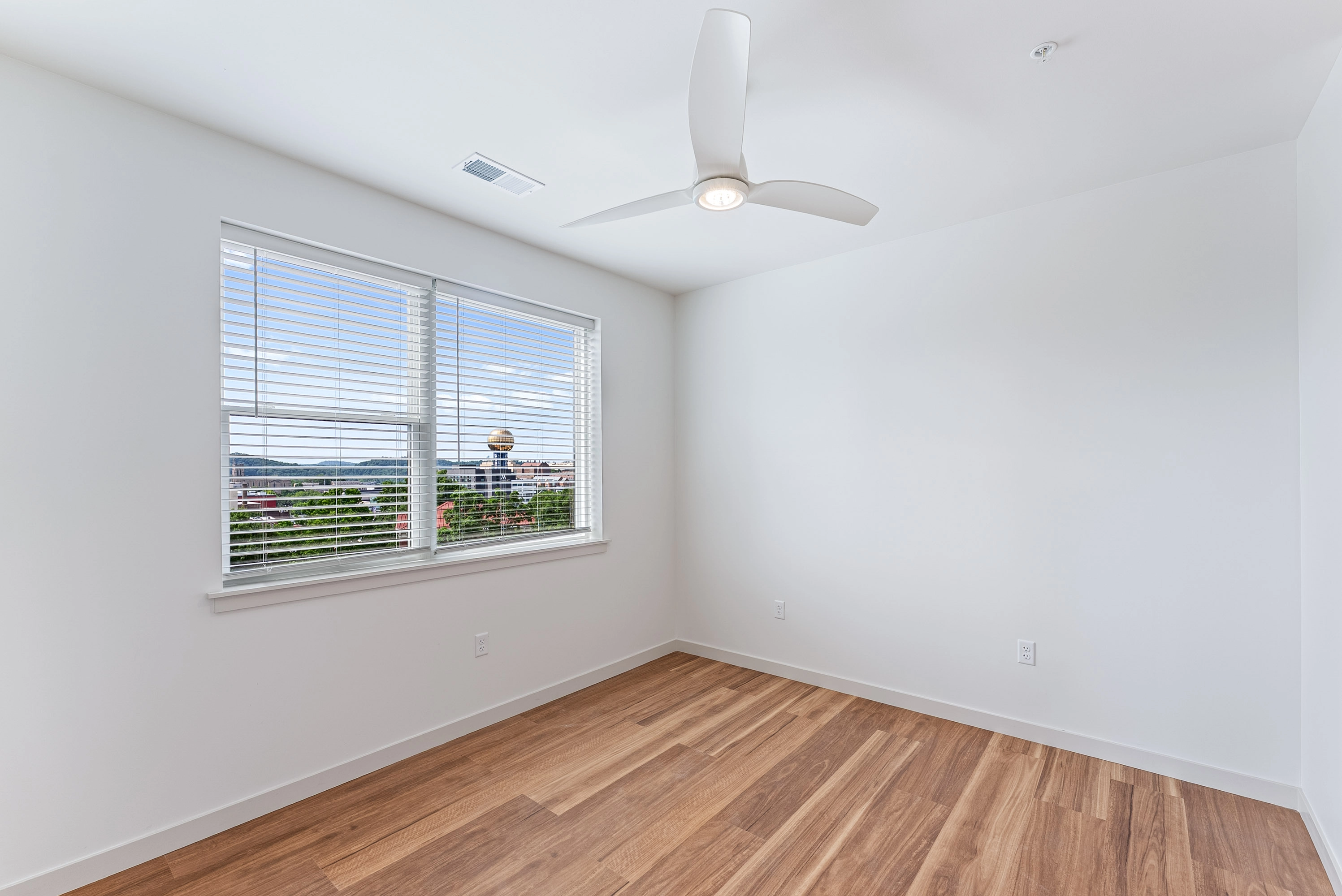 a bedroom with wooden flooring and a window that has open blinds