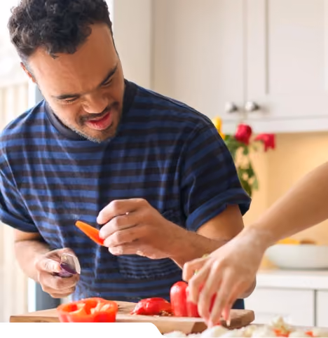 A man preparing vegetables at a kitchen counter alongside a support worker