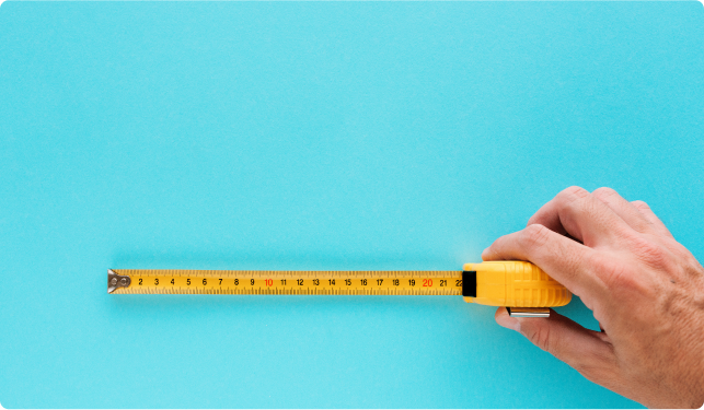 An image of a hand holding an partly unrolled yellow tape measure against a turquoise background