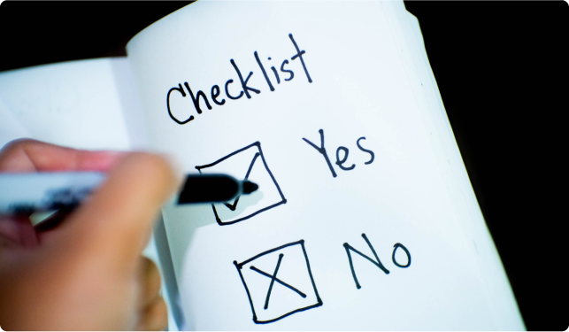 Hand holding a felt tipped pen above checkboxes labelled 'Yes and 'No' drawn in a notebook
