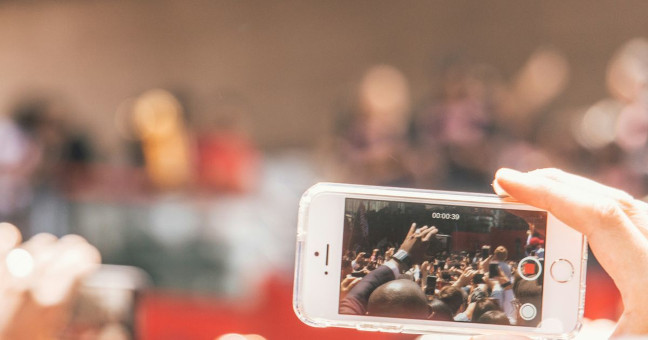 A hand holding a smart phone recording the crowd and stage in front
