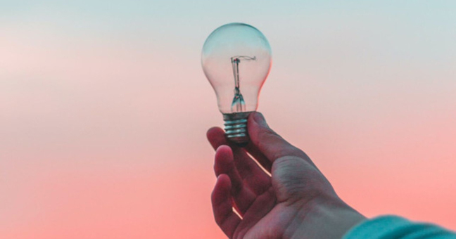 A hand holds out a lightbulb against a blue-to-pink gradient background