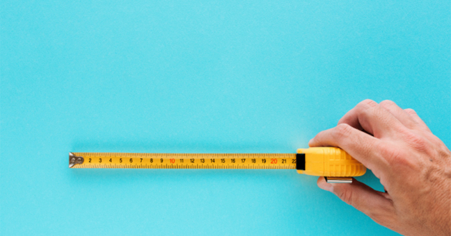An image of a hand holding an partly unrolled yellow tape measure against a turquoise background