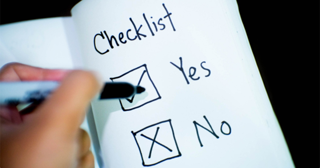 Hand holding a felt tipped pen above checkboxes labelled 'Yes and 'No' drawn in a notebook