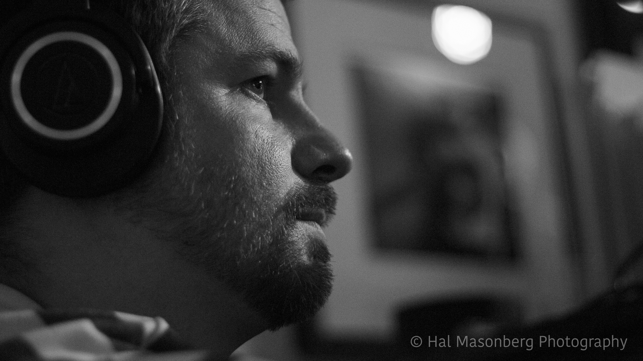 Close-up black and white profile of Ryan wearing headphones monitoring a live recording.
