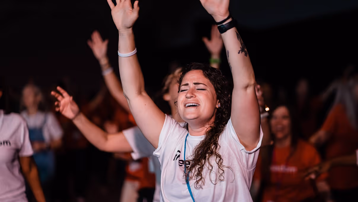 Woman with eyes closed and arms raised, expressing emotion at a crowded event.