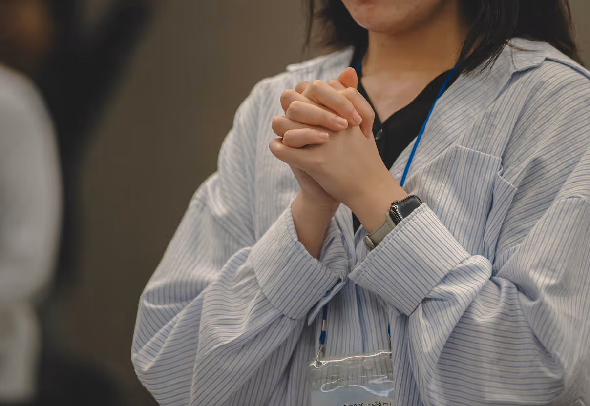 Person with clasped hands wearing a blue lanyard and a striped shirt.