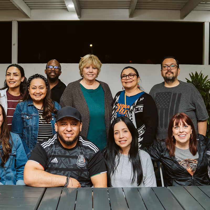 Group of diverse adults smiling and posing together outdoors at night under a covered patio.