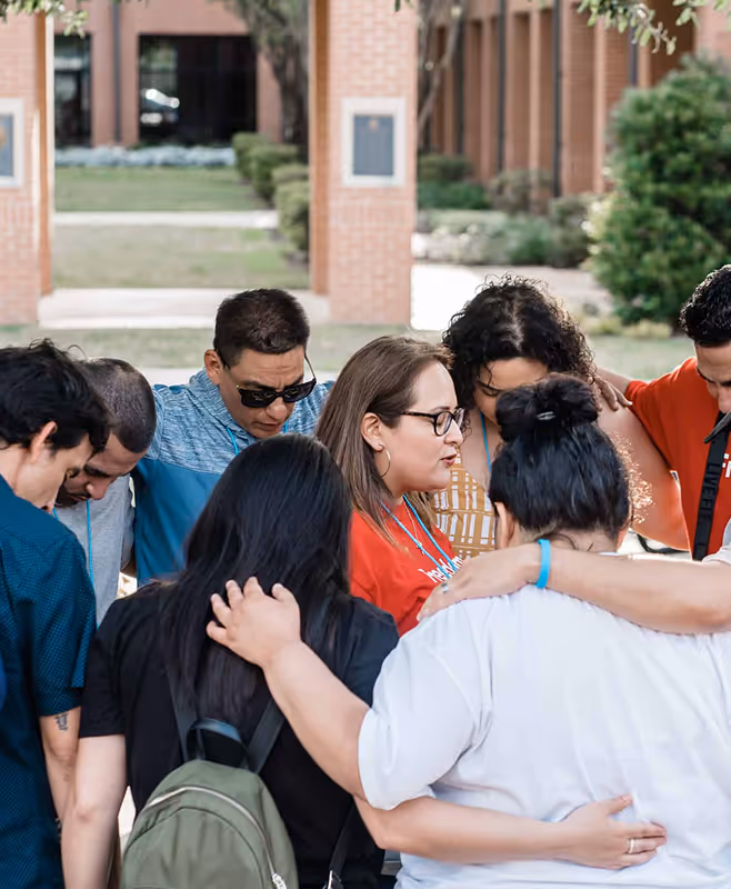 Group of diverse people standing close together in a huddle outdoors, showing support and unity.
