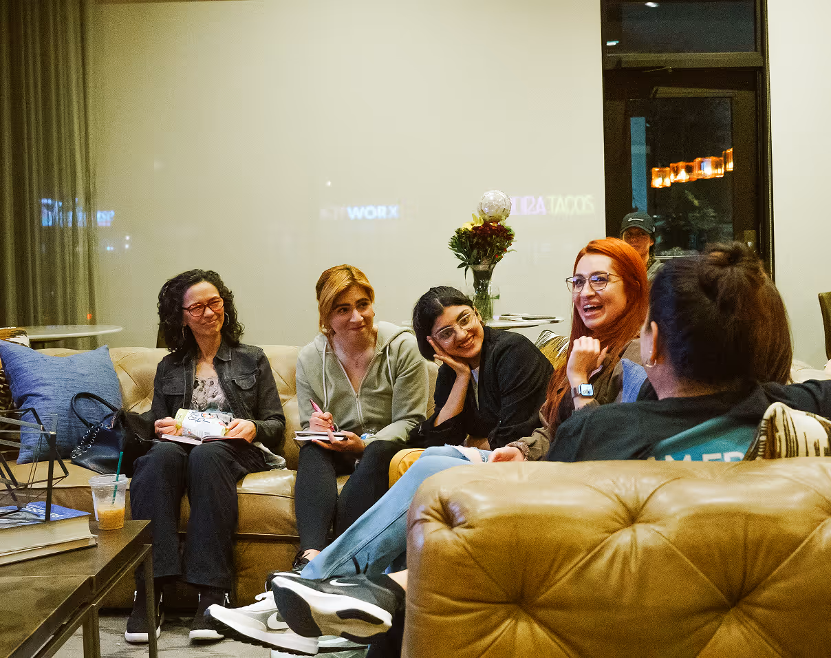 Five people sitting on couches in a cozy living room, engaged in conversation and smiling.