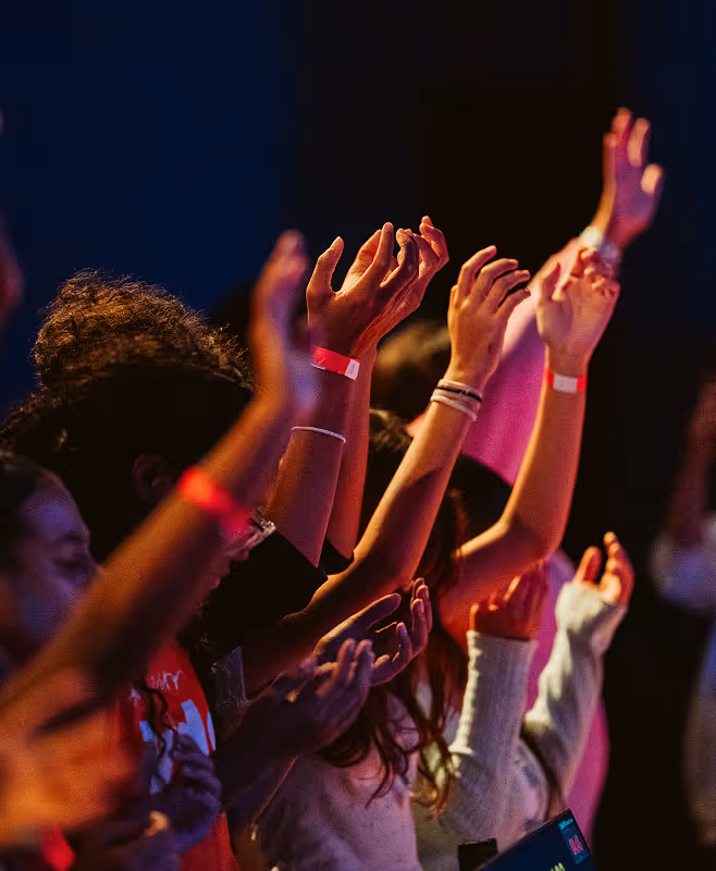 Group of people with raised hands engaged in worship or a concert under colorful lighting.