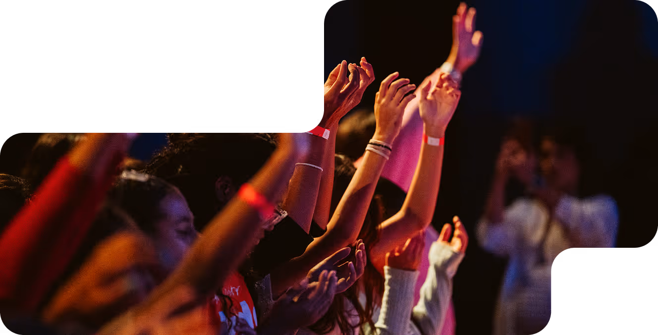 Group of people with raised hands engaged in worship or a concert under colorful lighting.