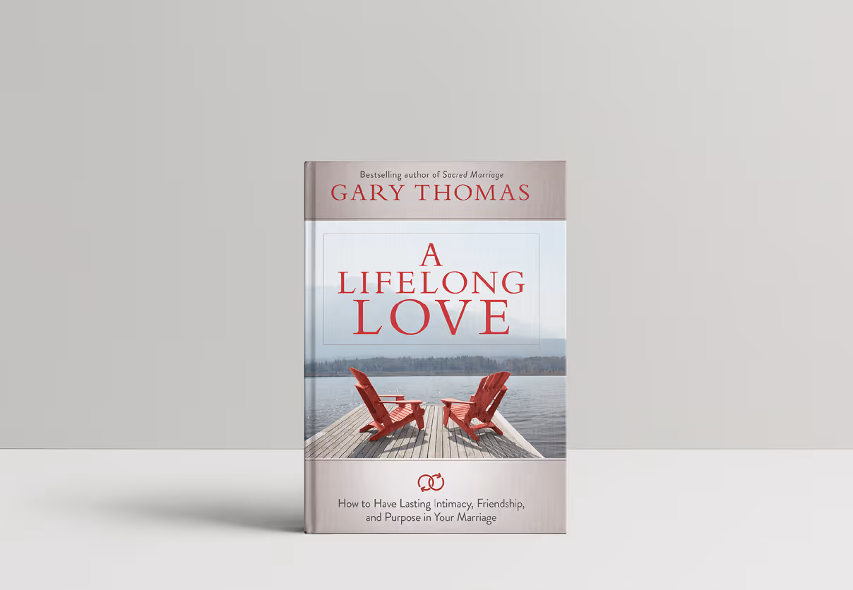 Book cover of 'A Lifelong Love' by Gary Thomas with two red chairs on a dock overlooking a lake and mountains.