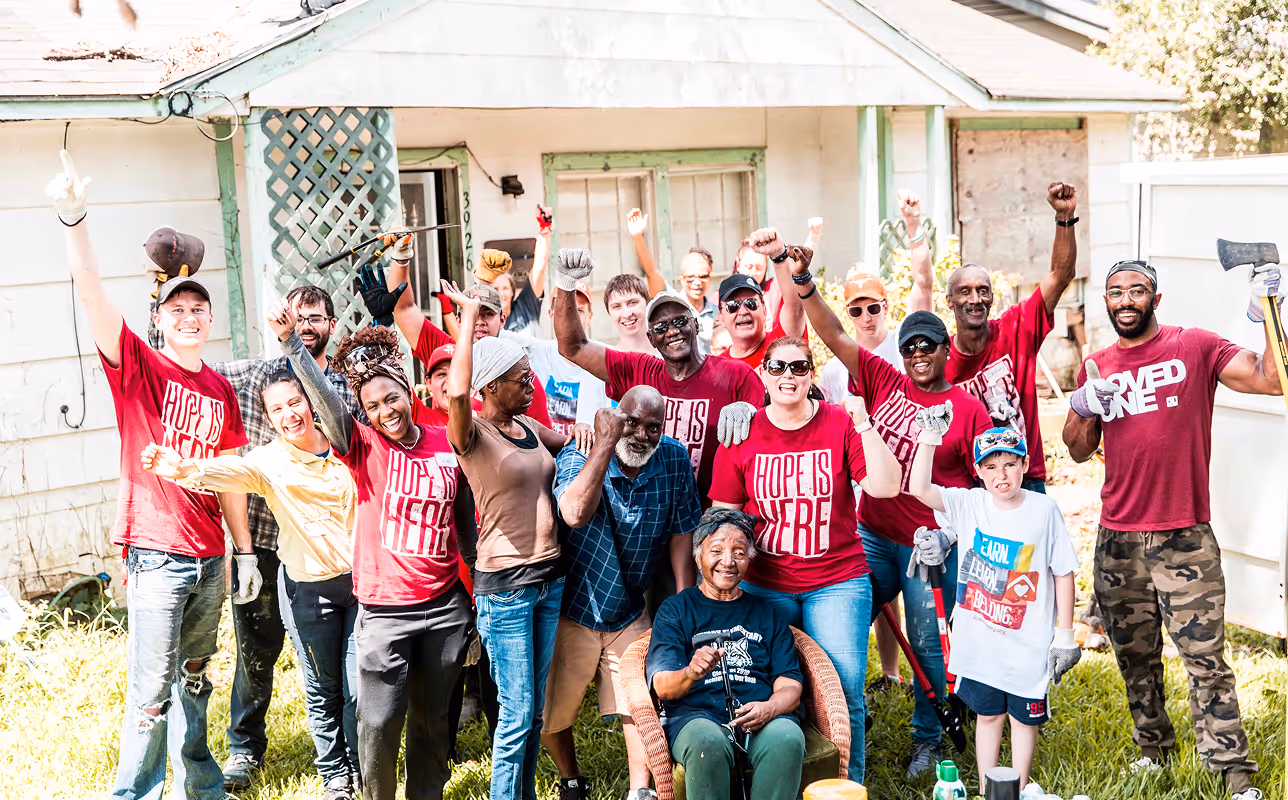 Group of diverse volunteers cheering and raising fists in front of a house during a community service event.