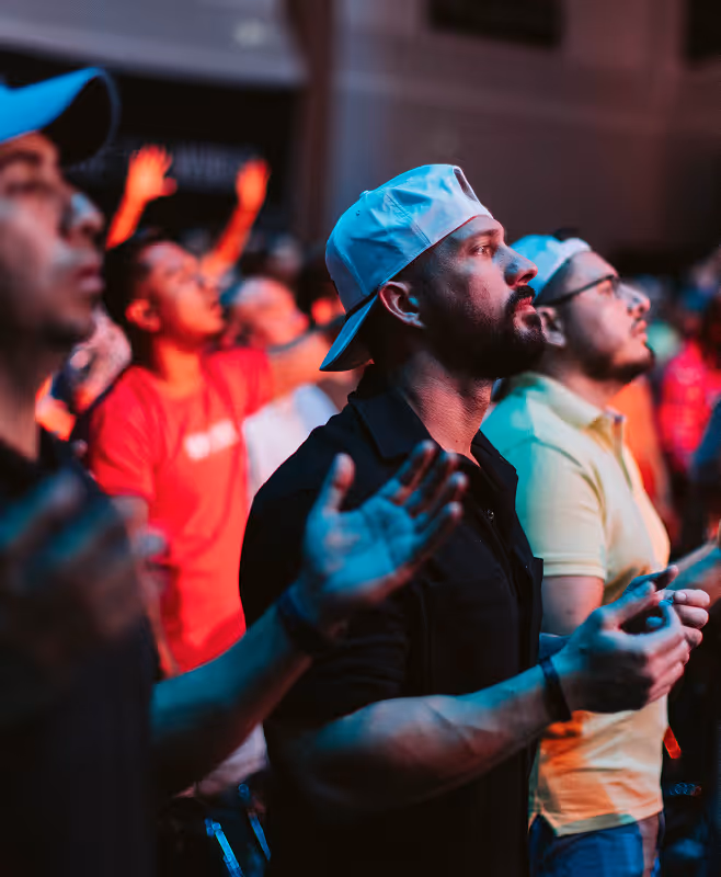 Men standing with eyes closed and hands raised in a crowd, appearing to be praying or worshiping.
