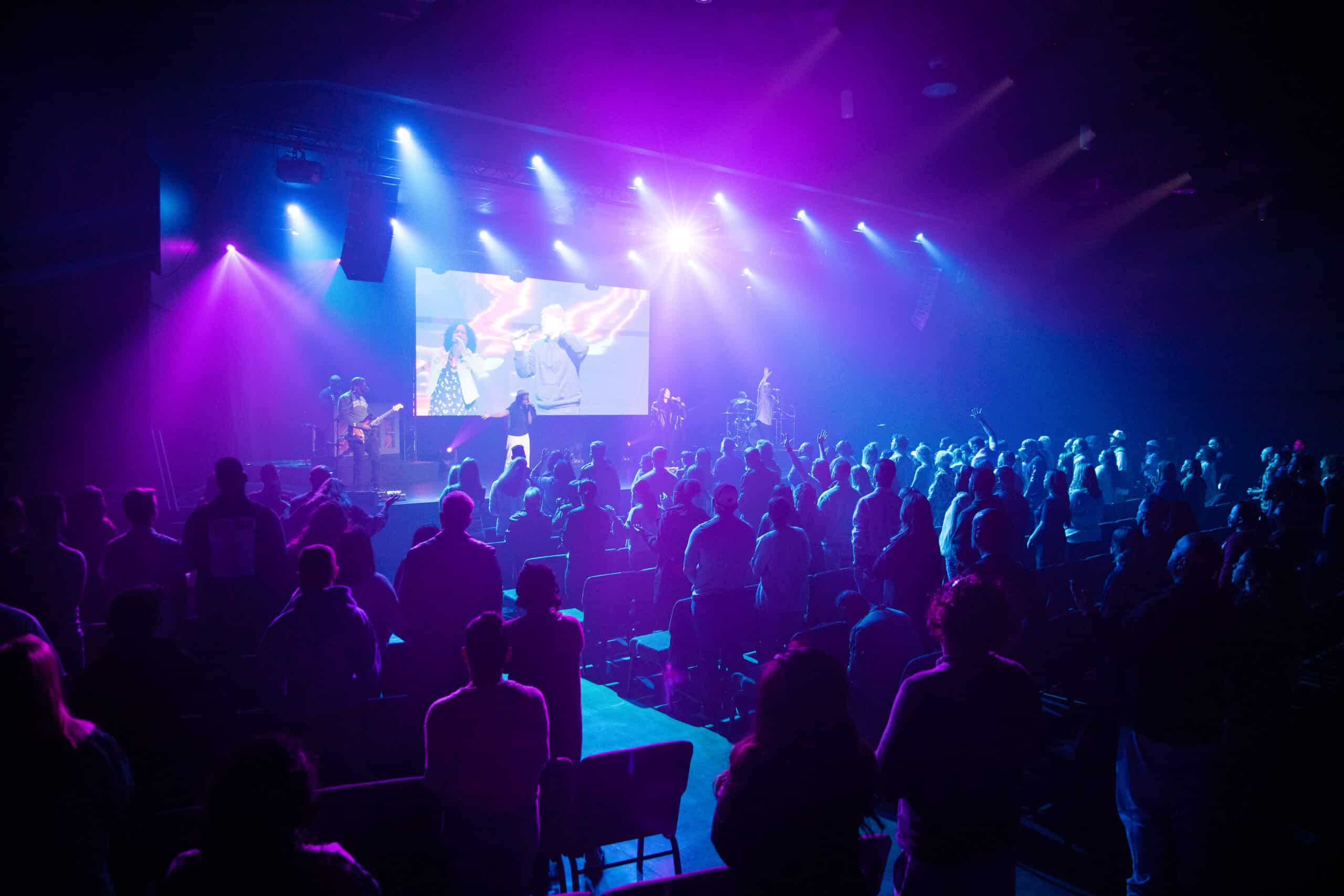 Crowd watching a live concert with purple and blue stage lighting and singers performing on stage.