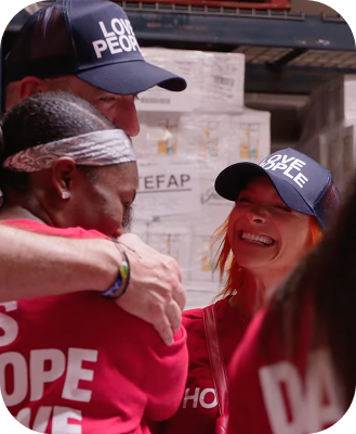 Three people wearing red shirts and navy hats smiling and hugging in a friendly embrace.