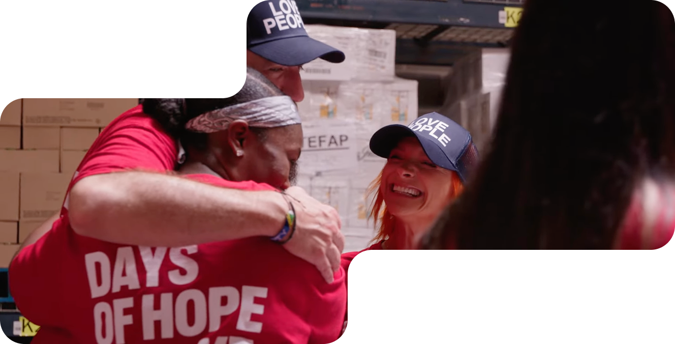 Three people hugging and smiling in a warehouse, wearing caps that say Love People and a shirt saying Days of Hope.