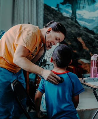 Woman wearing an orange shirt using a stethoscope to check a boy in a blue shirt's back indoors.