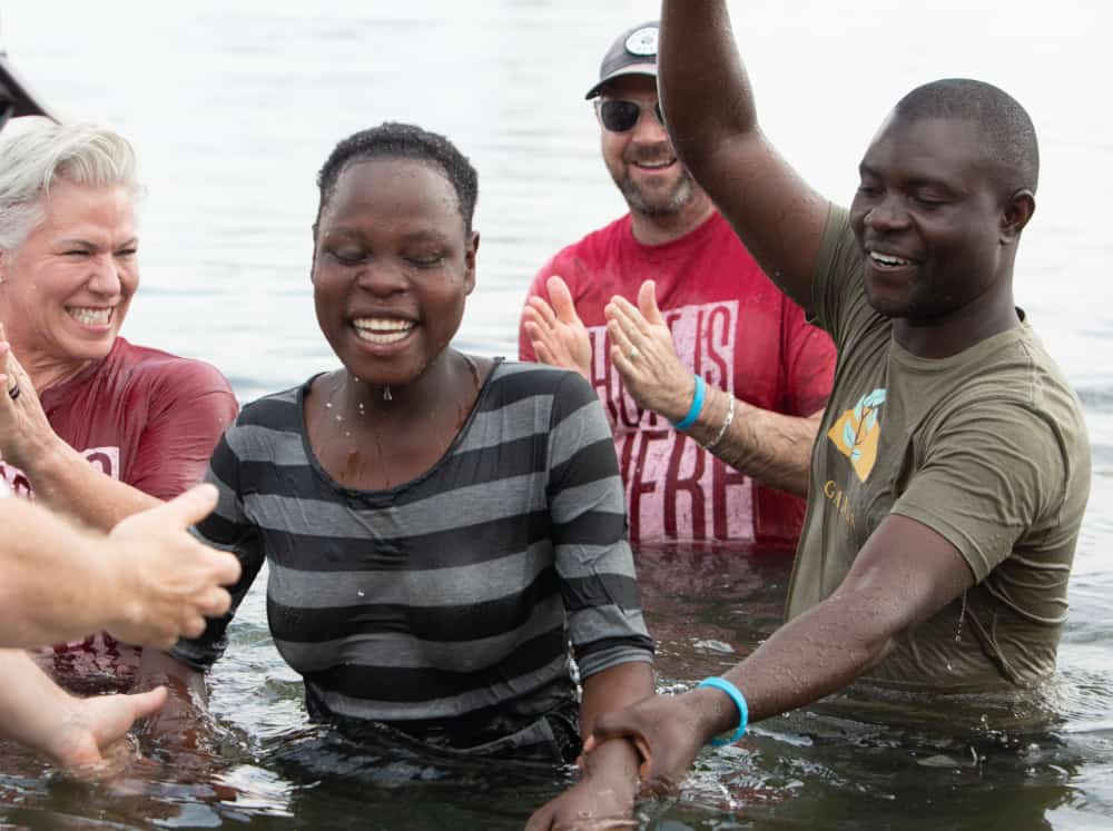 Group of diverse people smiling and celebrating a woman in water, possibly after a baptism or swim.