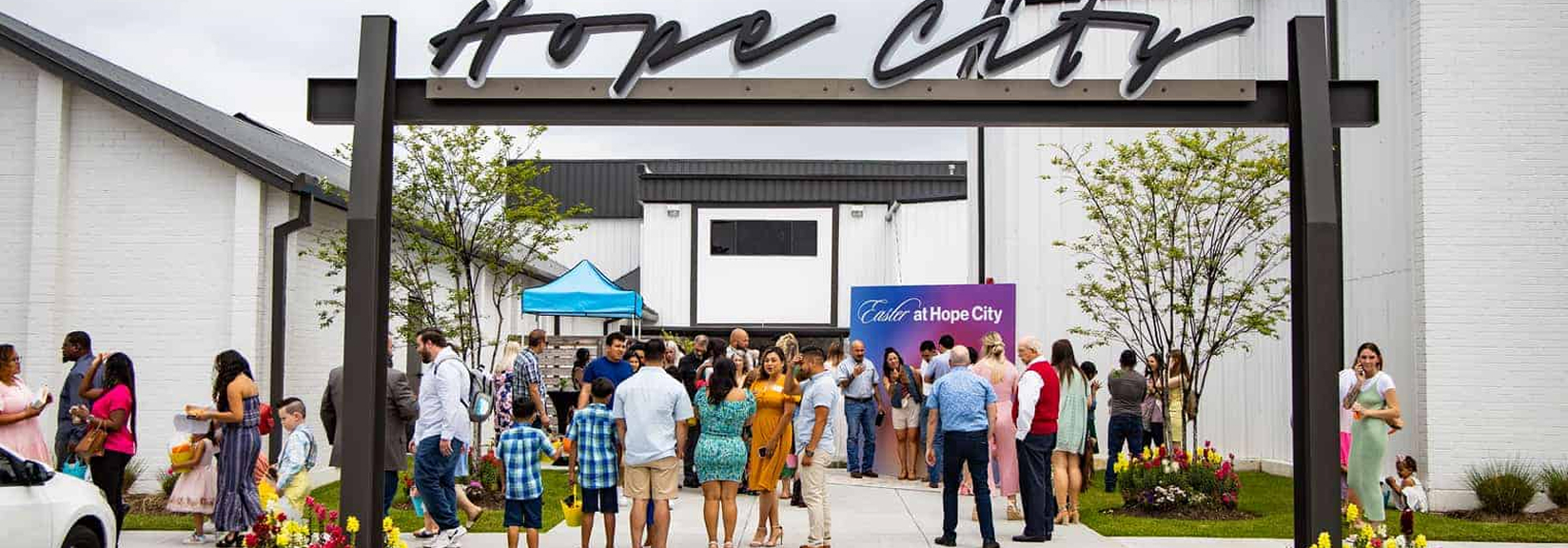 Group of people, including children, gathered outdoors under a Hope City sign for an Easter event.