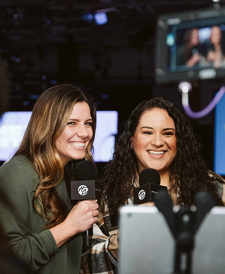 Two women smiling and holding microphones during a video recording session.
