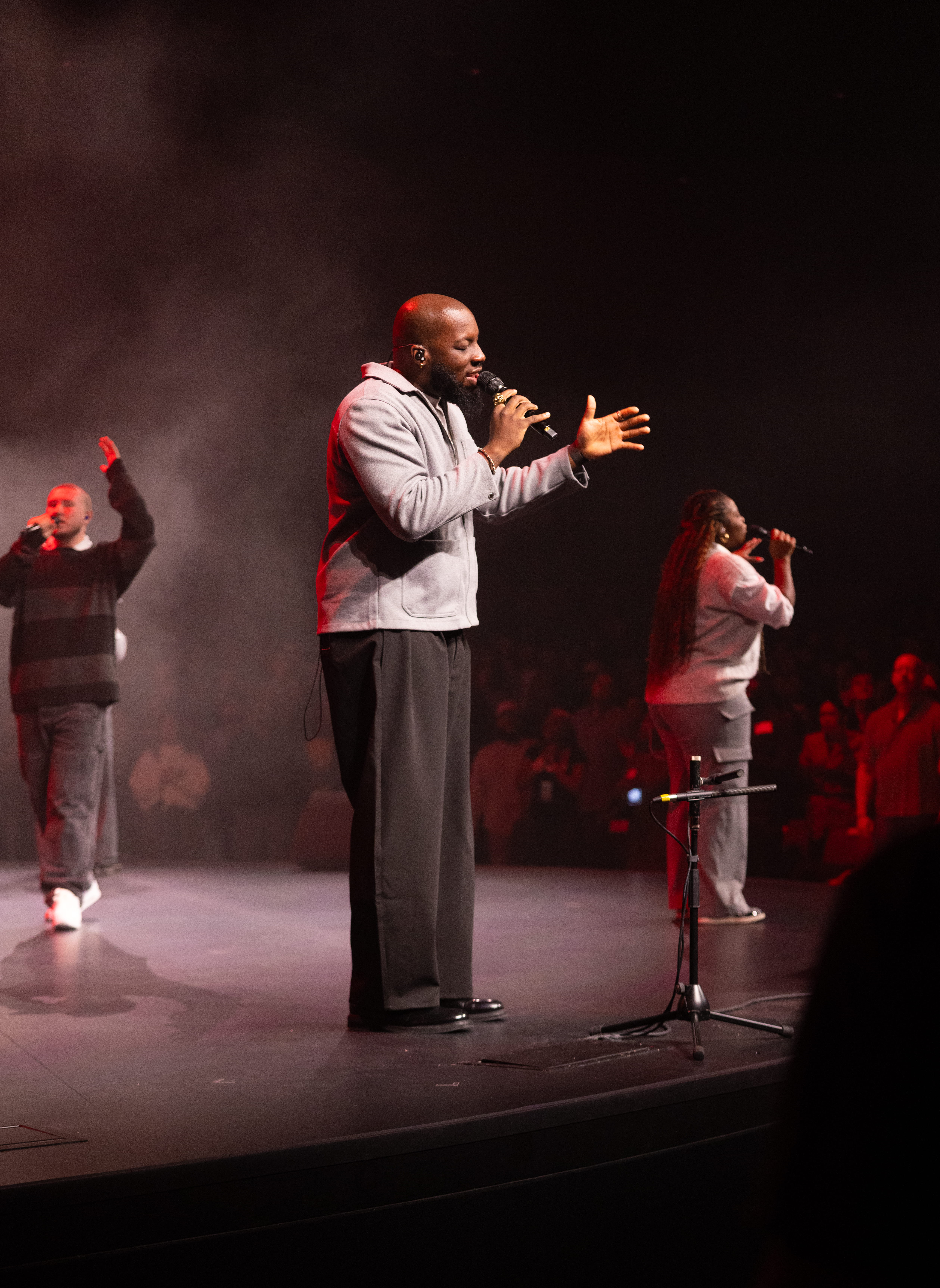 Worship band performing on stage with large screen and audience in a church setting.