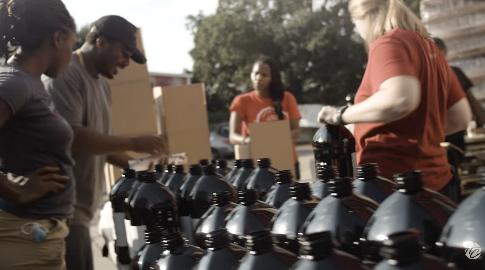 Volunteers distributing food and supplies at an outdoor relief tent near a brick building.