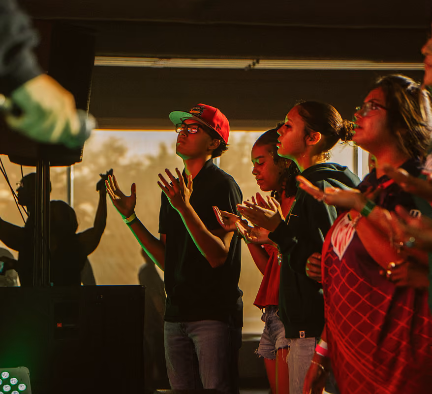 Group of young people with eyes closed and hands raised, engaged in worship or a spiritual gathering.