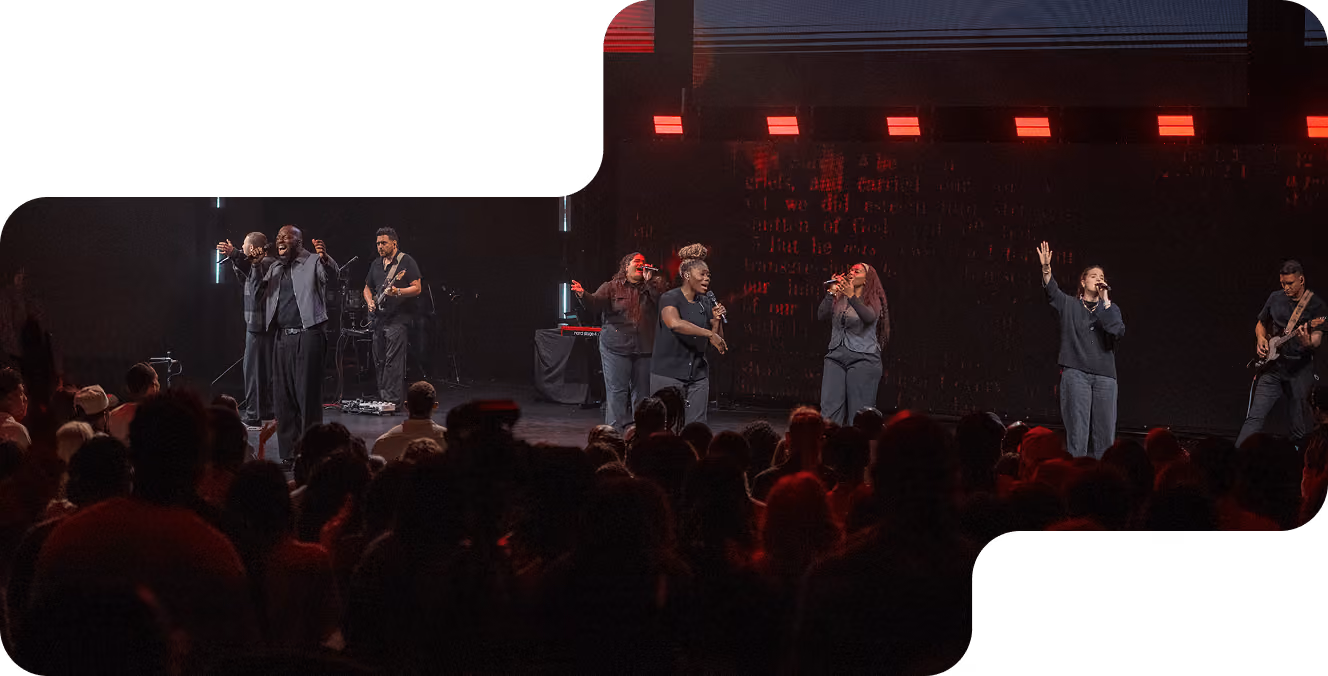 Musician playing electric guitar passionately on stage during a live performance with singers in background.