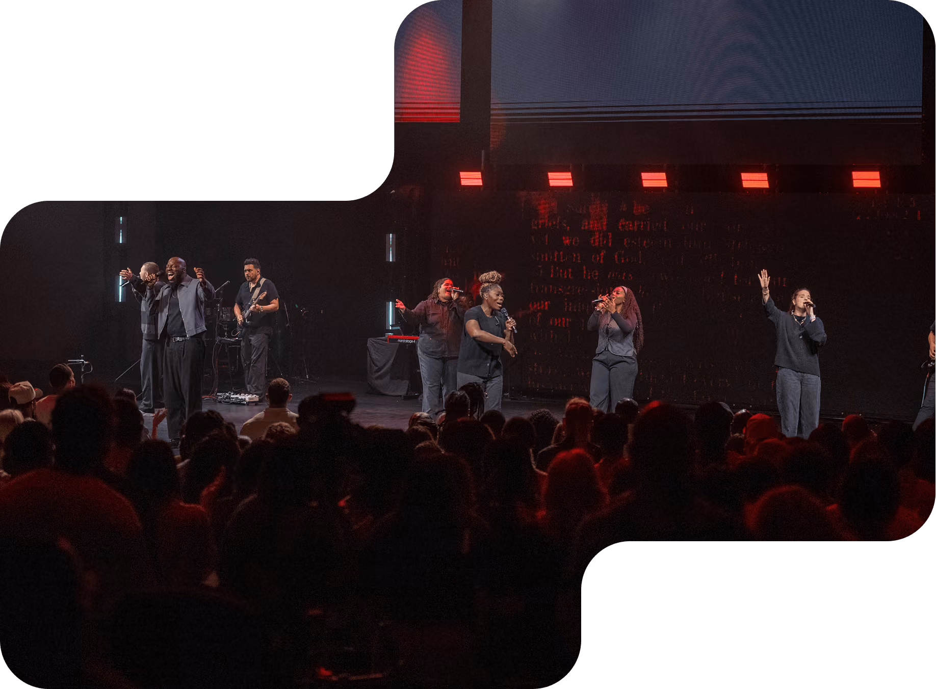 Musician playing electric guitar passionately on stage with backup singers and blue lighting.