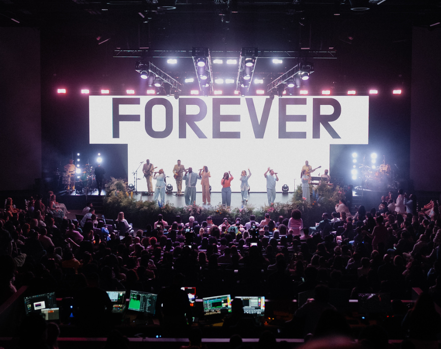 Band performing live on stage with singers and guitarists in front of an audience at a concert.