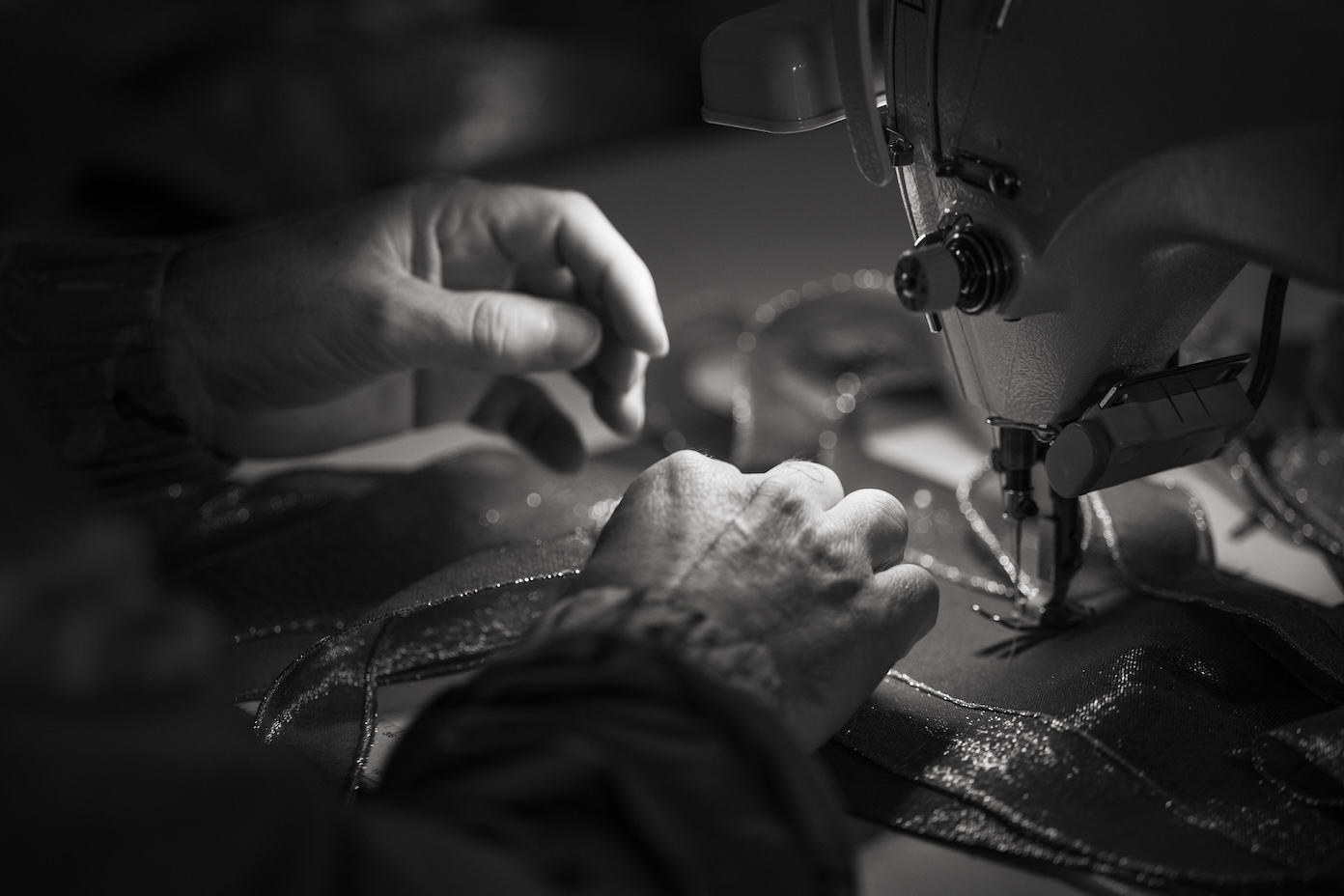 Close-up of hands guiding fabric under a sewing machine needle in black and white.
