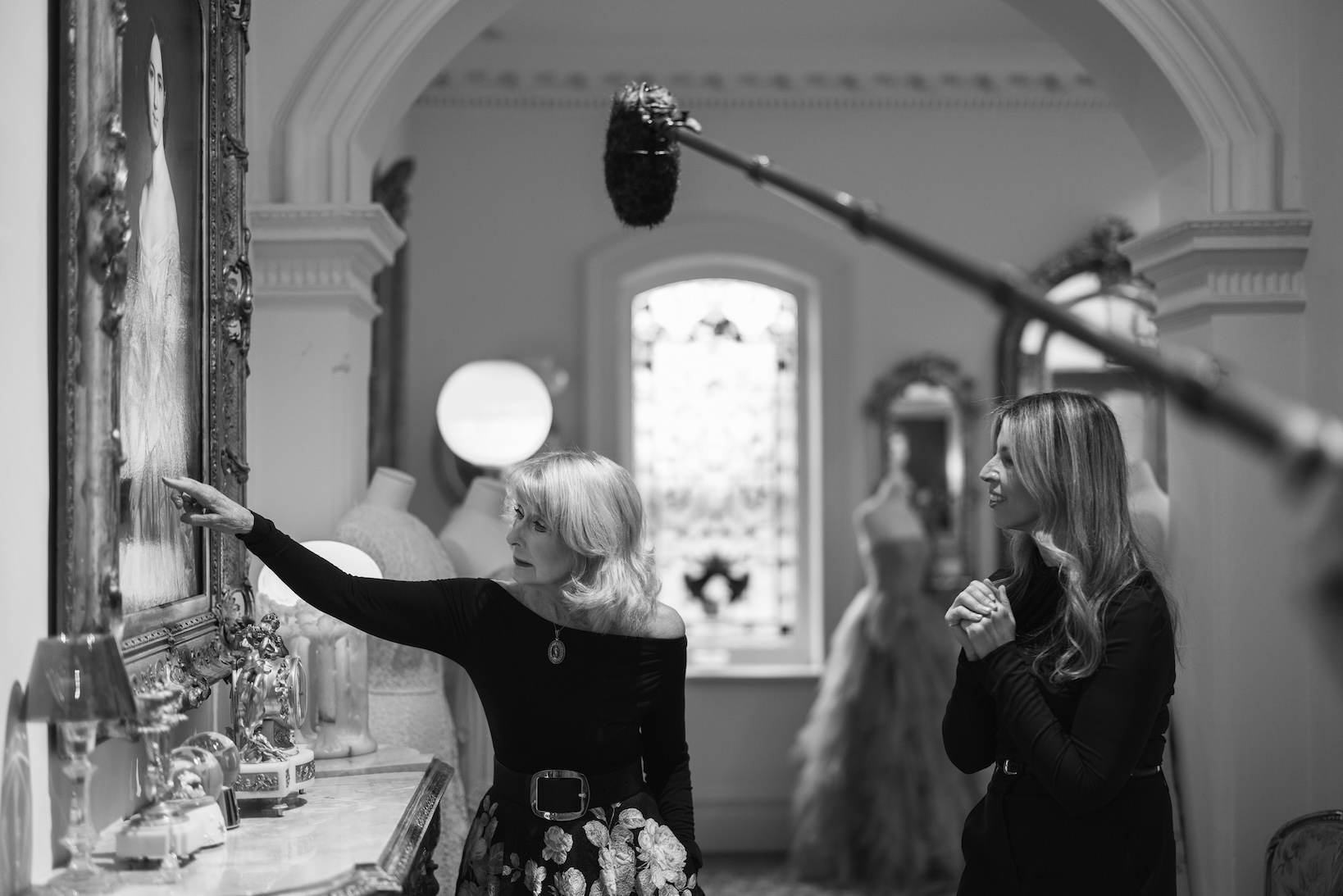 Krystyna Campbell-Pretty AM & Helen Mantzis in elegant black outfits stand in a vintage room with framed paintings behind them.