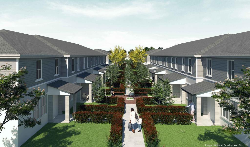 Walkway lined with bushes and trees between rows of modern two-story townhouses with grey roofs, showing people walking and entering homes.