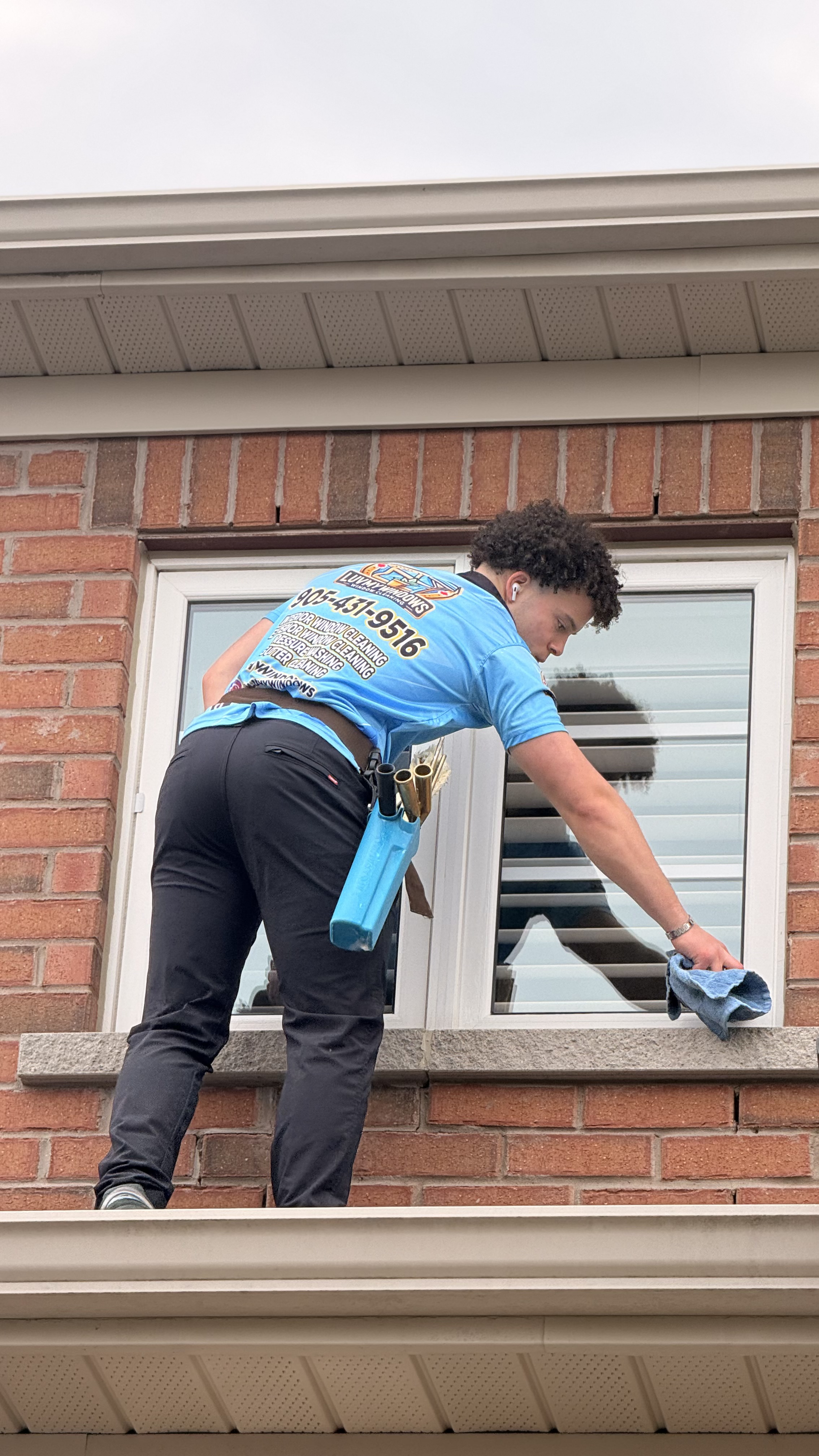 Long-handled brush with water tubes cleaning a wet glass window on a building exterior.