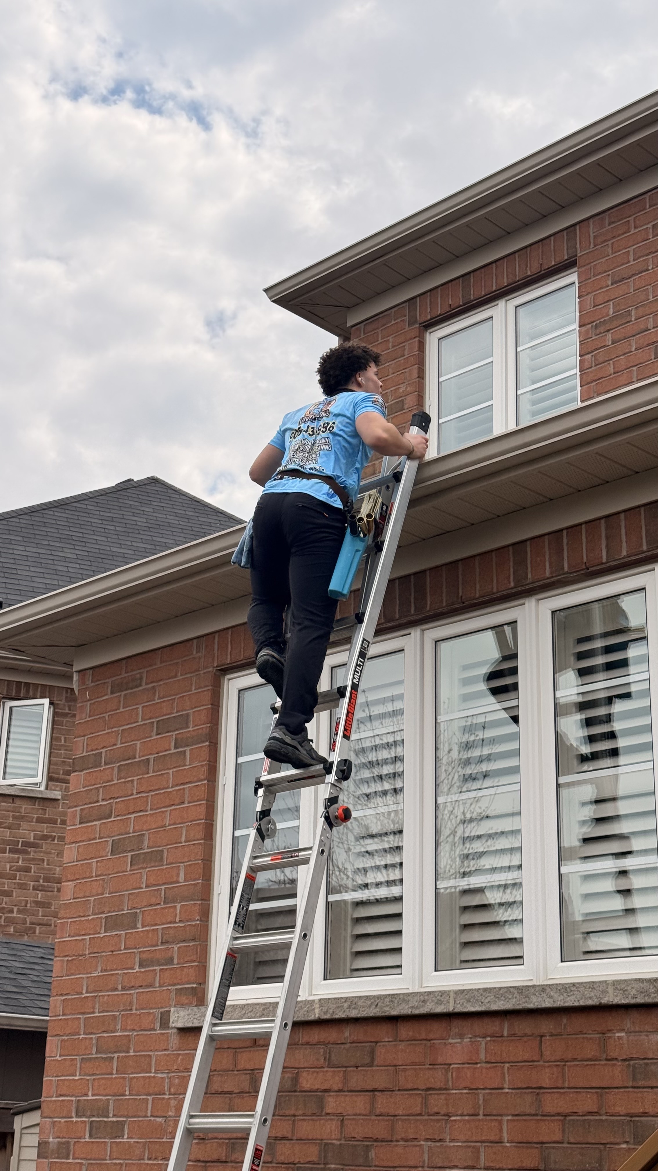 Person on ladder cleaning or reaching towards an outdoor wall light on a wooden patio structure at dusk.