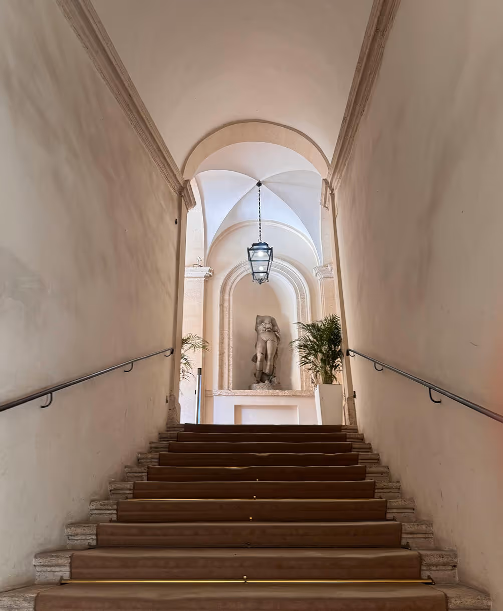 Stone staircase leading up to a niche with a statue, flanked by two potted plants and illuminated by a hanging lantern.